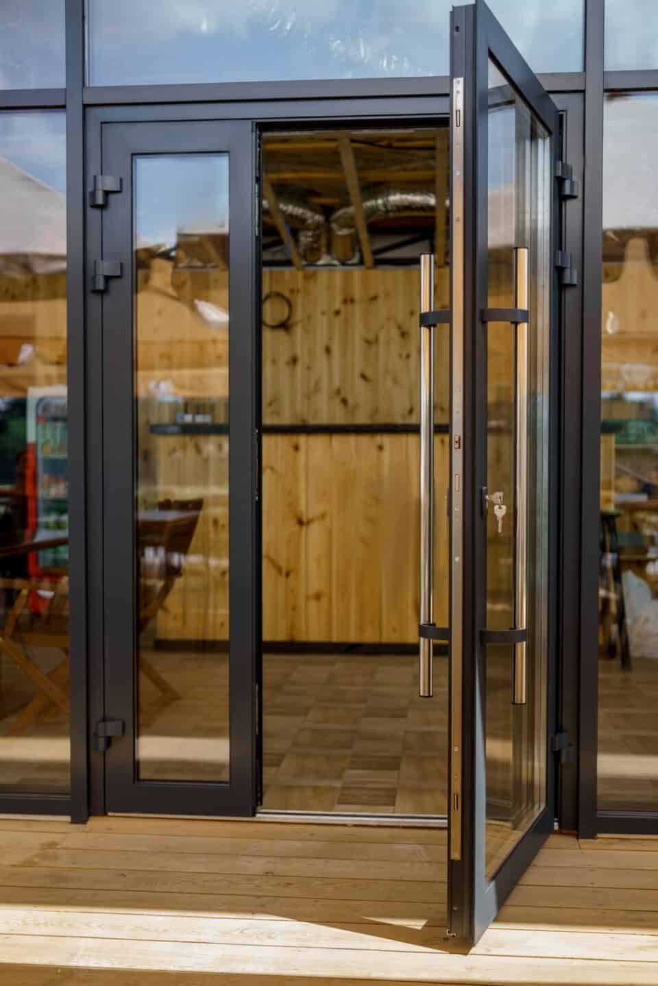 A glass door with a metal frame is slightly ajar, hinting at the work of a professional locksmith. Inside, a wooden interior reveals tables and chairs, inviting you to enter.