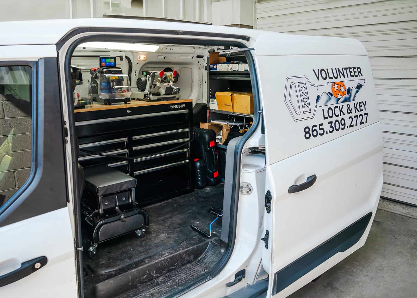 Open the side door of a van to reveal locksmith tools and key cutting equipment inside. The van's exterior prominently displays "Volunteer Lock & Key" with a phone number, showcasing their expertise as a trusted commercial locksmith.